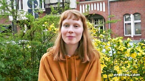 Smiling freckled redhead babe in orange hoodie posing outdoors with yellow flowers