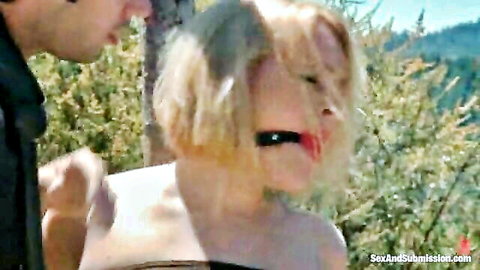 Blonde submissive ball gagged outdoors in rough BDSM domination with man