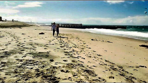 Romantic couple walks hand-in-hand on sunny beach towards ocean waves