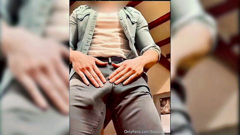 Muscular young man teasing huge cock bulge in tight grey pants with hands on belt