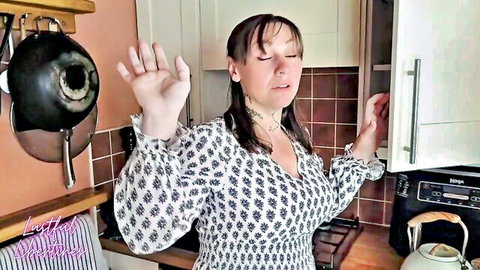 MILF babe with big tits raises arms teasing in kitchen wearing patterned blouse