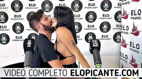 Busty Latina passionately kissing bearded guy in black top on Elo Picante podcast set