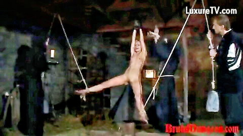 Naked blonde suspended spread-eagle in dungeon bondage by cloaked doms exposing tits and pussy