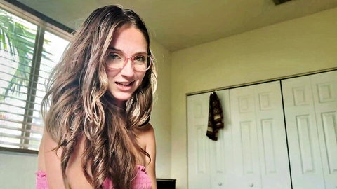 Brunette teen with glasses smiles while exposing her small perky tits topless in bedroom