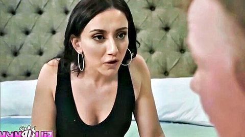 Brunette stepmom in tight black tank top, big tits spilling out, surprised face on bed