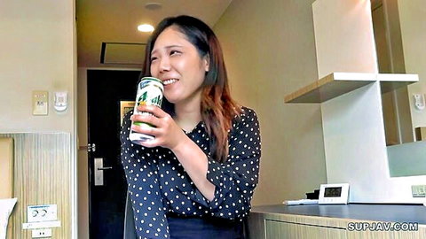Smiling Asian woman in polka-dot blouse holds green drink can in hotel room