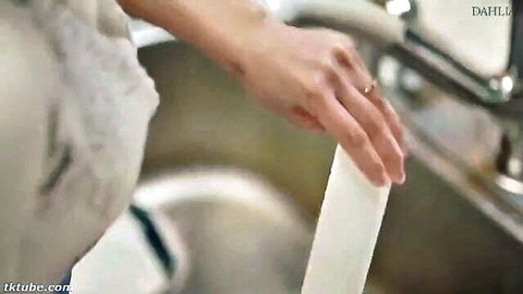 Woman's hand with wedding ring squeezing white tube over kitchen sink.