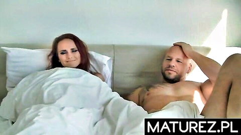 Redhead MILF smiles with bald hunk husband in bed sheets teasing naked bodies