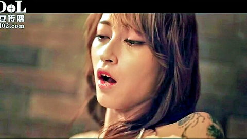 Seductive Asian woman with tattoos, wavy brown hair, teasing open mouth close-up