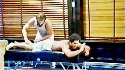 Shirtless muscular hunk massages friend's ass in tight white shorts on table