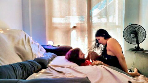 Goth singer with dark hair seducing purple-haired woman on bed