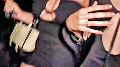 Close-up of women's elegant hands with rings holding beige purse and cocktail glass at dimly lit party.