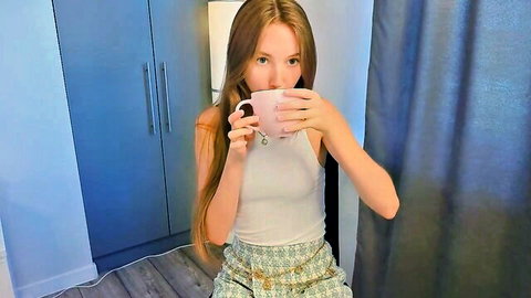 Redhead webcam babe sips pink mug in tight white tank top showing cleavage solo