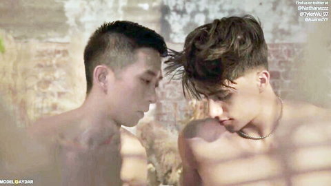 Two shirtless young Asian guys in passionate gay eye contact against brick wall