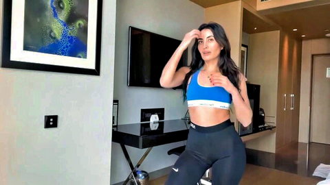 Sexy brunette influencer teasing in blue Calvin Klein bra and tight black Nike yoga pants in hotel room