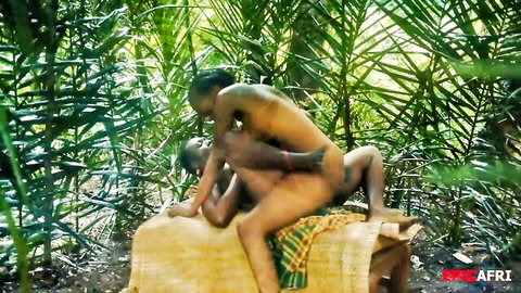 Nude black man thrusting cock into ebony woman's pussy on jungle mat amid palms