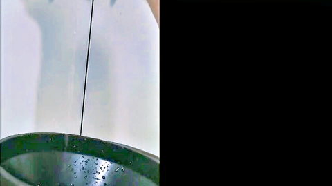Hand dangling thin wire into green bowl of water droplets close-up view