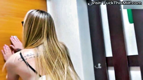 Blonde MILF bends over orange door in black bra showing big juicy ass and shoulder tattoo from behind.