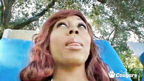 Mature black cougar with curly red hair looks up ecstatically with open mouth during outdoor blowjob