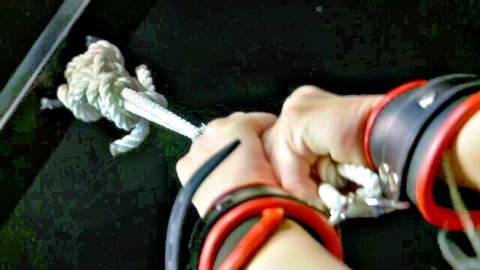 Woman's wrists bound in red cuffs and white rope for BDSM punishment