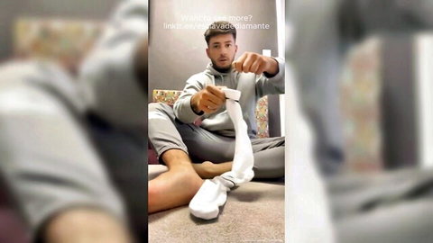 Gay guy in hoodie plays with white knee socks showing sweaty socked feet