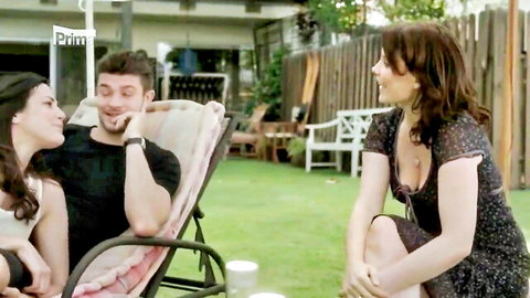 Brunette MILF in low-cut floral dress flirts with smiling hunk on lounge chair while dark-haired friend watches outdoors