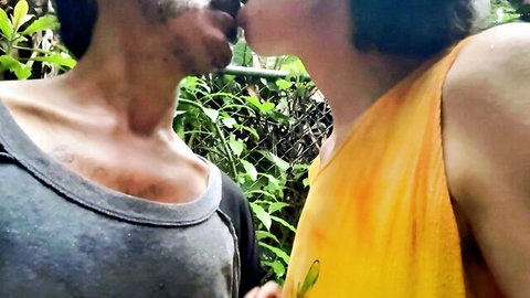 Bearded man passionately kissing mature woman outdoors amid lush greenery