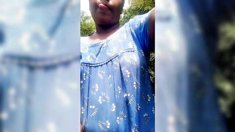 Playful ebony teen sticks tongue out seductively in blue floral dress outdoor selfie