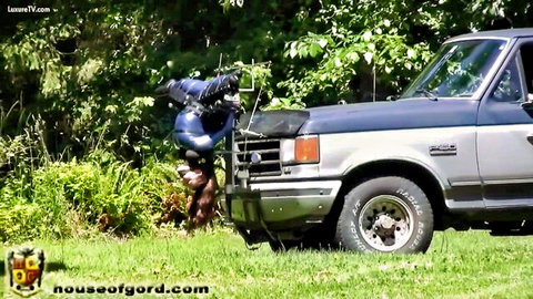 Woman in blue latex suspended over truck in outdoor fuckmachine BDSM scene