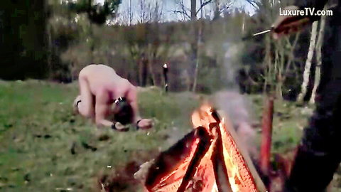Danish femdom outdoor branding: bound nude woman kneels near fire as man holds hot iron