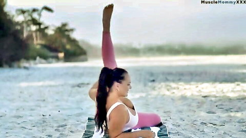 Curvy brunette in white crop top and pink yoga pants doing flexible beach stretch