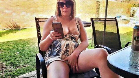 Curvy blonde in floral dress teasing outdoors with phone, legs spread