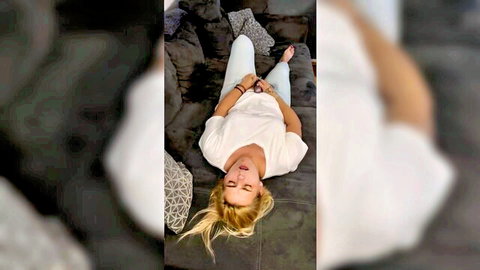 Blonde woman aroused on couch, white top and pants, seductive pose