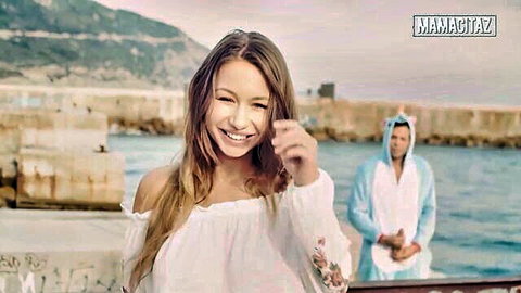 Smiling playful brunette babe in off-shoulder white top pointing teasingly outdoors at harbor