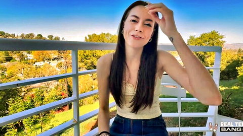Selena Love smiling on sunny balcony in yellow top and jeans