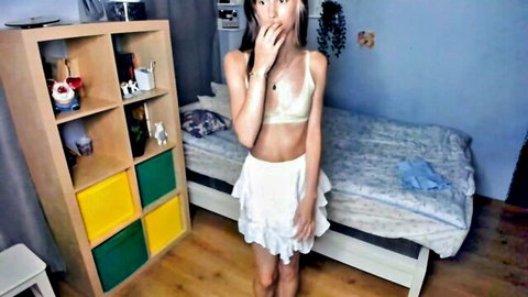 Skinny teen in skimpy white bralette showing underboob and frilly mini skirt teases with open mouth in bedroom webcam