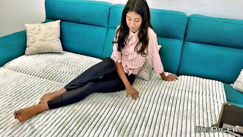 Sexy brunette lounging barefoot on turquoise bed in pink shirt and tight black pants
