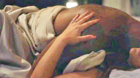 White woman grips bald black man's head passionately under sheets in bed