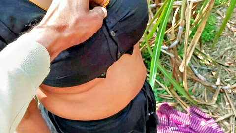 Busty South Asian woman's black top pulled exposing underboob and belly by man's hand in outdoor sugarcane field