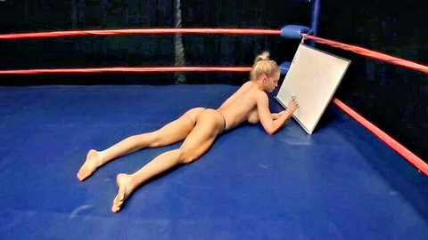 Ana Foxxx nude in catfight wrestling pose, prone on mat writing on board