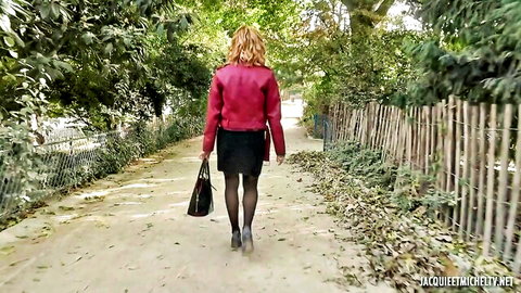 Blonde woman in red jacket, black skirt, stockings walking outdoors