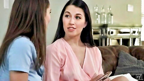 Two slim young women in sexy tops chatting intimately on couch