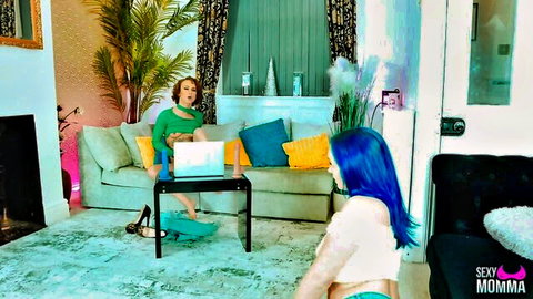 Blue-haired woman in lingerie teases seated friend on laptop in playful lesbian scene