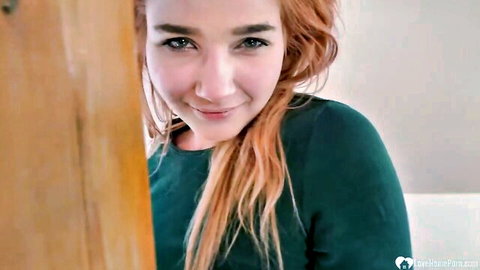 Smiling redhead woman peeking from door in green top, teasing solo play
