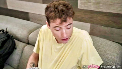 Young curly-haired guy in yellow t-shirt on couch with mouth open in pleasure