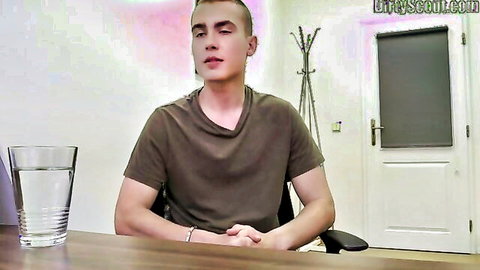 Young twink in green t-shirt sits smiling at desk with water glass on webcam