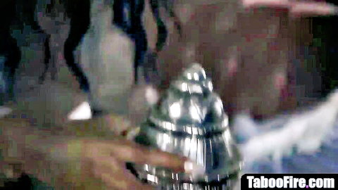 Black TV hostess hand grips shiny metallic dildo in explicit scene