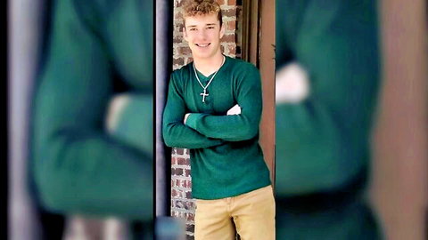 Young blonde curly haired jock in green sweater, arms crossed smiling confidently