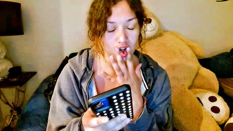 Scarlett licks lips seductively holding phone in open hoodie, teasing huge boobs