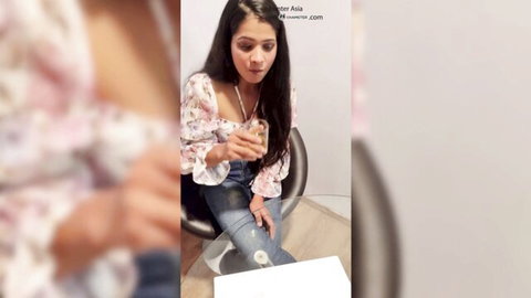Sexy young Asian brunette with deep cleavage in low-cut floral top sitting on chair holding drink